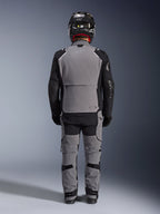 Alpinestars Andes Pro Drystar® XF Jas, achteraanzicht, donkergrijze en zwarte adventure touring uitrusting, gedragen met bijpassende grijze en zwarte broek, zwarte carbon helm en zwarte handschoenen, voorzien van technische panelen en reflecterende branding