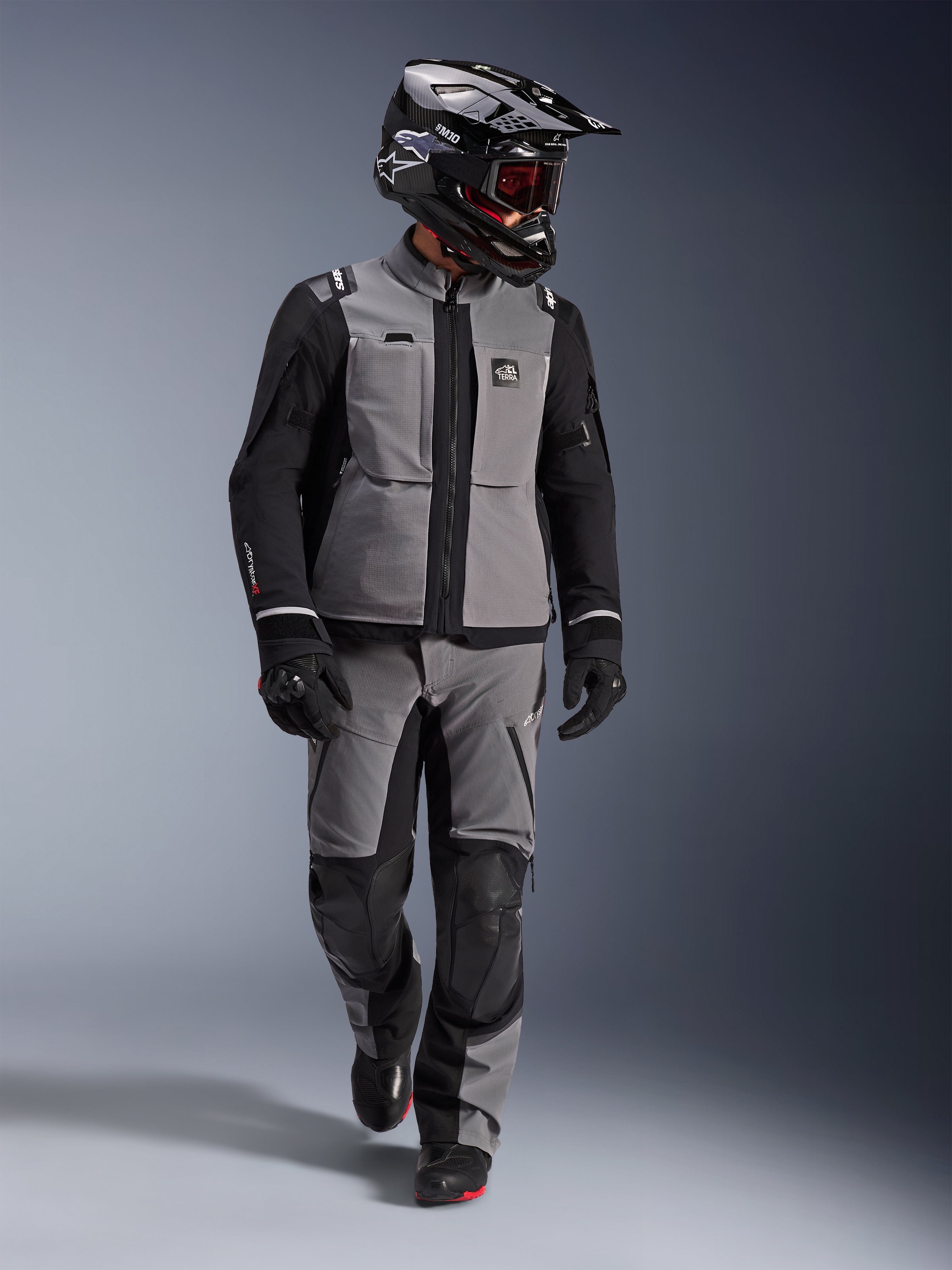Adventure-rijder in Alpinestars Andes Pro Drystar® XF Jas in donkergrijs en zwart, bijpassende adventure-broek, zwarte Alpinestars-helm met bril, zwarte handschoenen en laarzen, complete technische touring-uitrusting voor lange afstanden