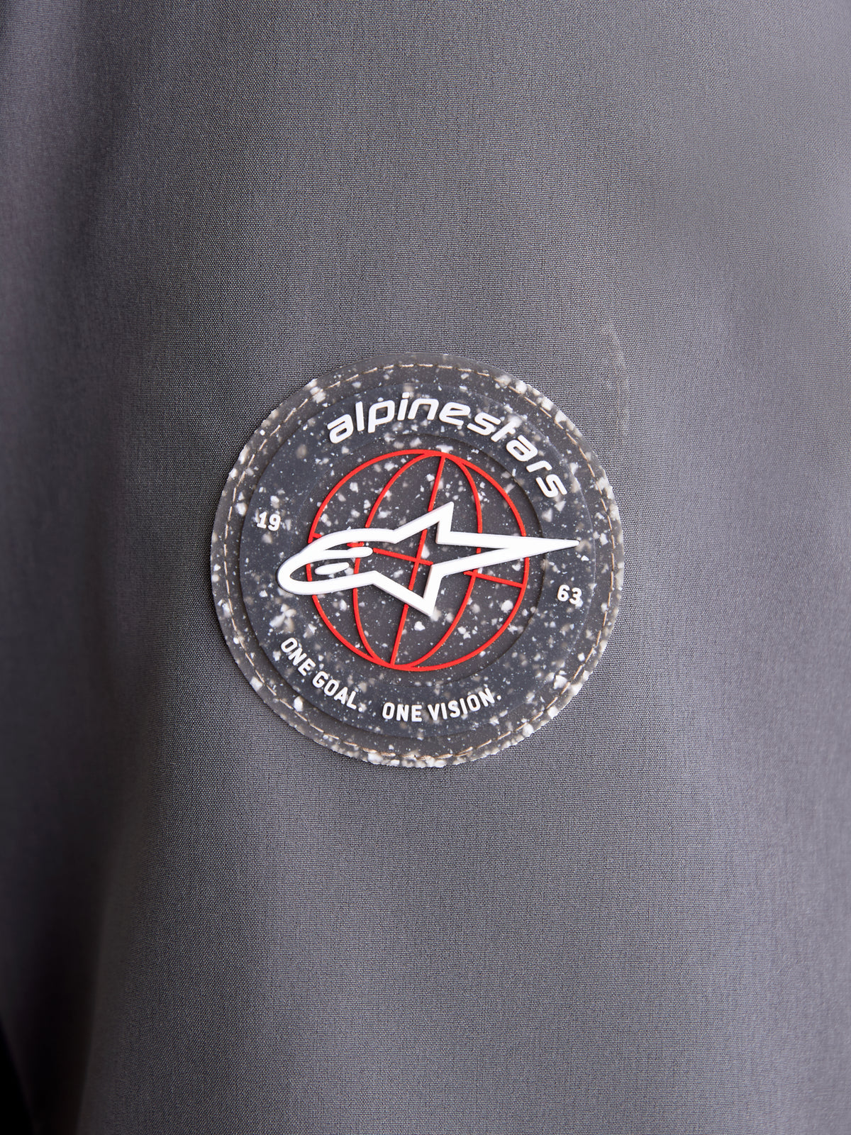Alpinestars Therma-Tech WP Jack, close-up van de ronde merkpatch op de donkergrijze en zwarte textielmouw, met het A-star embleem en de kenmerkende branding