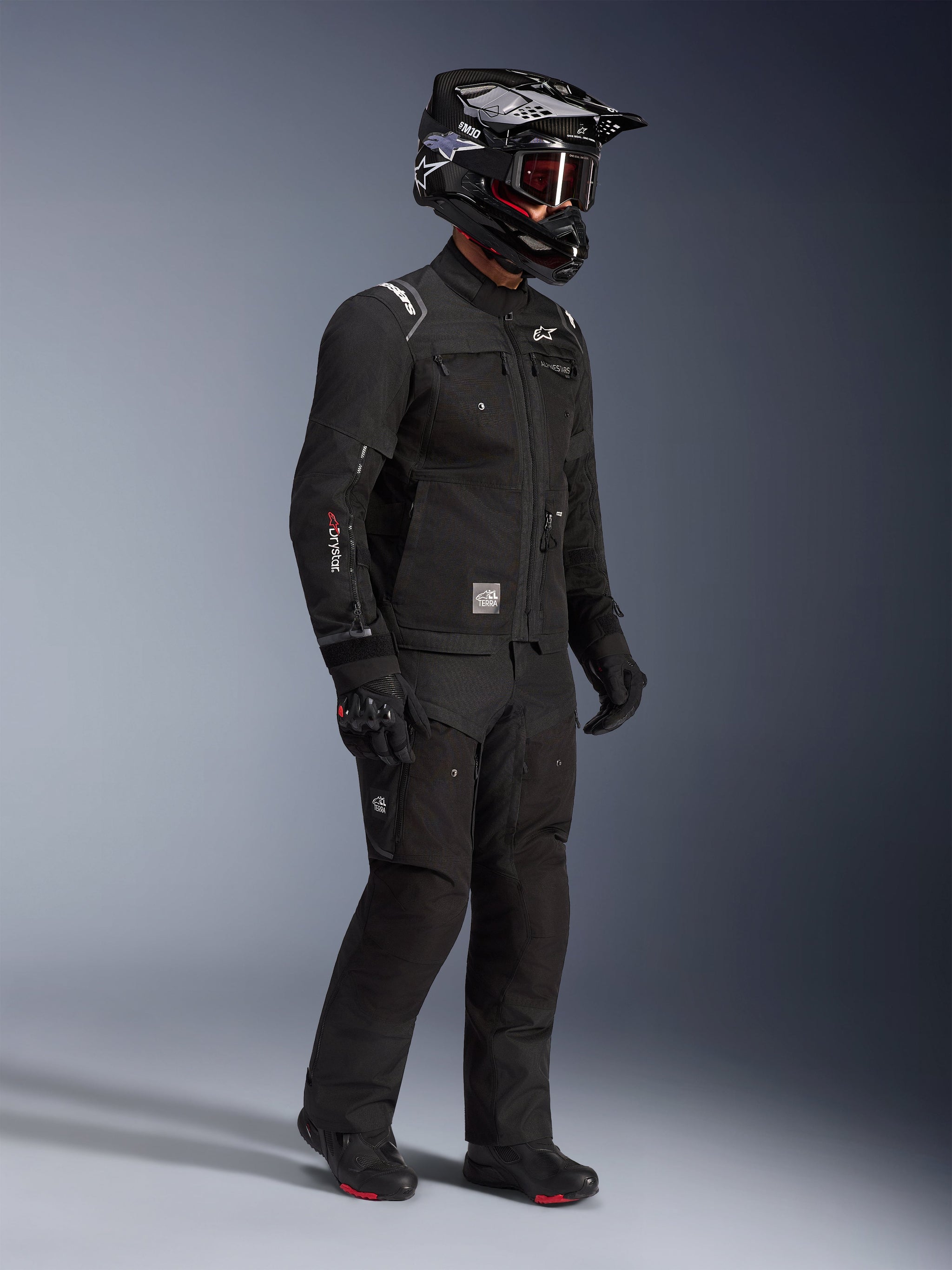Alpinestars Cusco Drystar® Jacket, Black adventure touring motorcycle jacket, worn with matching black pants and a full-face helmet with goggles, featuring a functional multi-pocket design, technical textile construction, and Drystar branding on the sleeve.