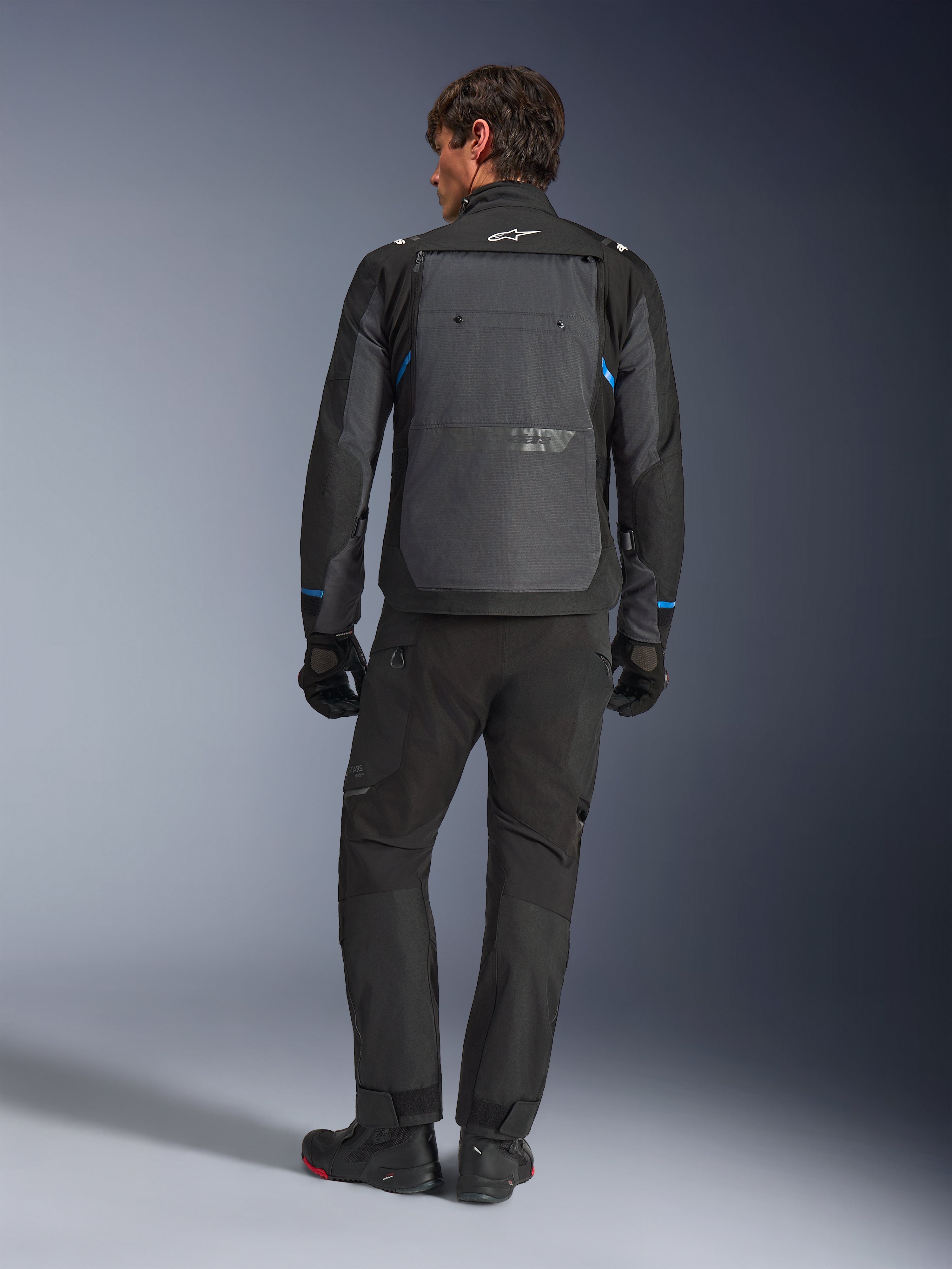 Alpinestars Cusco Drystar® Jacket, Black and Deep Gray with blue accents, rear view, worn with matching black adventure pants and gloves, featuring a large gray back panel and white logo on the collar, designed for road and adventure touring
