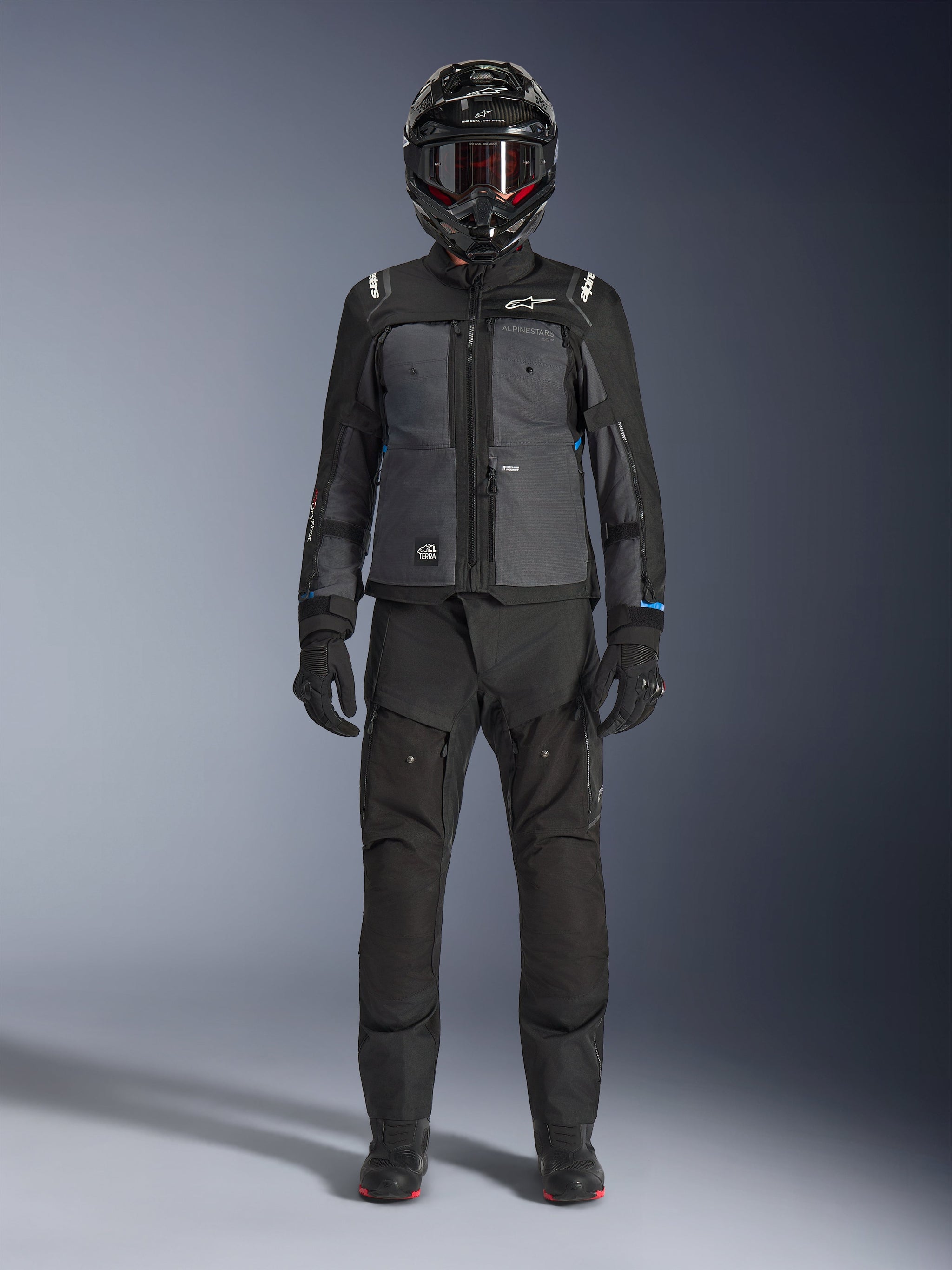Alpinestars Cusco Drystar® Jas, zwart en donkergrijs adventure touring jack, gedragen met bijpassende zwarte broek, handschoenen en een integraalhelm, volledig vooraanzicht, beschermende motorkleding