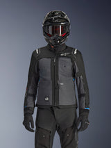 Alpinestars Cusco Drystar® Jas, zwart en donkergrijs, adventure touring motorjas gedragen met bijpassende zwarte technische broek en een dual-sport helm, tweekleurig ontwerp met ripstop-panelen en Alpinestars-branding
