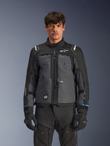 Alpinestars Cusco Drystar® jas, touring motorjas, zwart en diepgrijs, vooraanzicht op model, met Alpinestars-logo's op de borst en schouders, Drystar®-branding op de mouw, technisch ontwerp met meerdere zakken en ventilatieritsen, gecombineerd met zwarte motoruitrusting