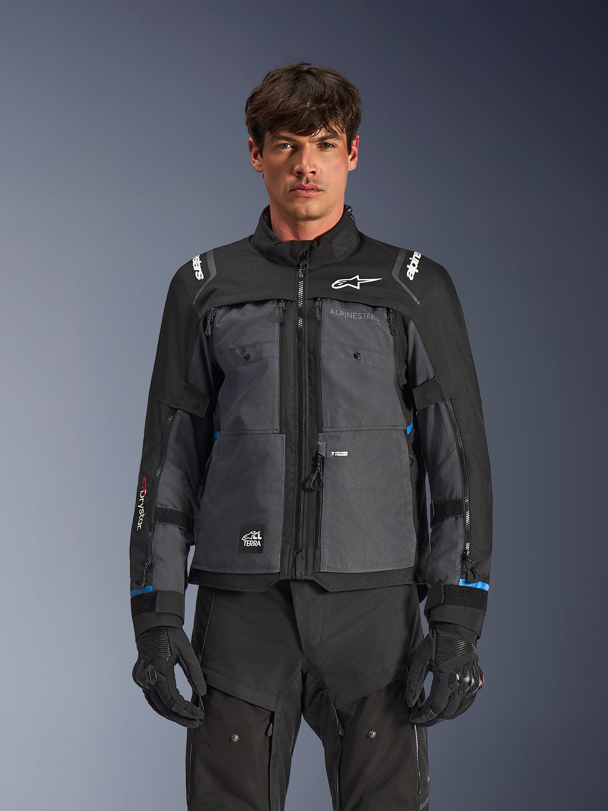 Alpinestars Cusco Drystar® jas, touring motorjas, zwart en diepgrijs, vooraanzicht op model, met Alpinestars-logo's op de borst en schouders, Drystar®-branding op de mouw, technisch ontwerp met meerdere zakken en ventilatieritsen, gecombineerd met zwarte motoruitrusting