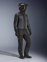 Model draagt Alpinestars Cusco Drystar® Jas in Black en Deep Gray, gecombineerd met volledige motoruitrusting inclusief een zwarte helm, bijpassende technische broek, handschoenen en laarzen, voorzien van een ripstop- en softshell-constructie voor weggebruik en adventure touring