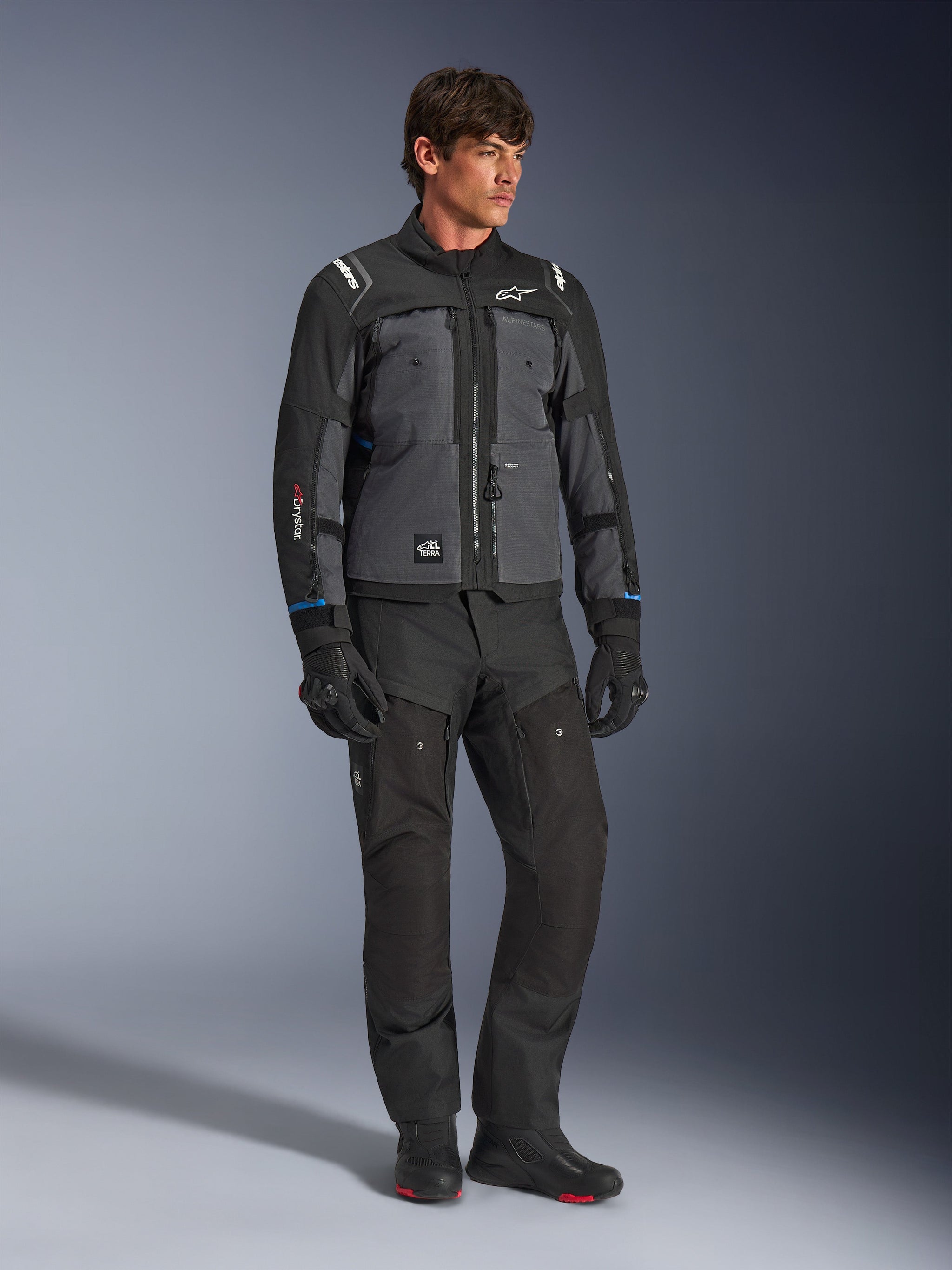 Alpinestars Cusco Drystar® Jas in zwart en diepgrijs, technische touring-motorjas met panelen in verschillende tinten, gedragen met bijpassende zwarte motorbroek en handschoenen, ontworpen voor road- en adventure-touring.