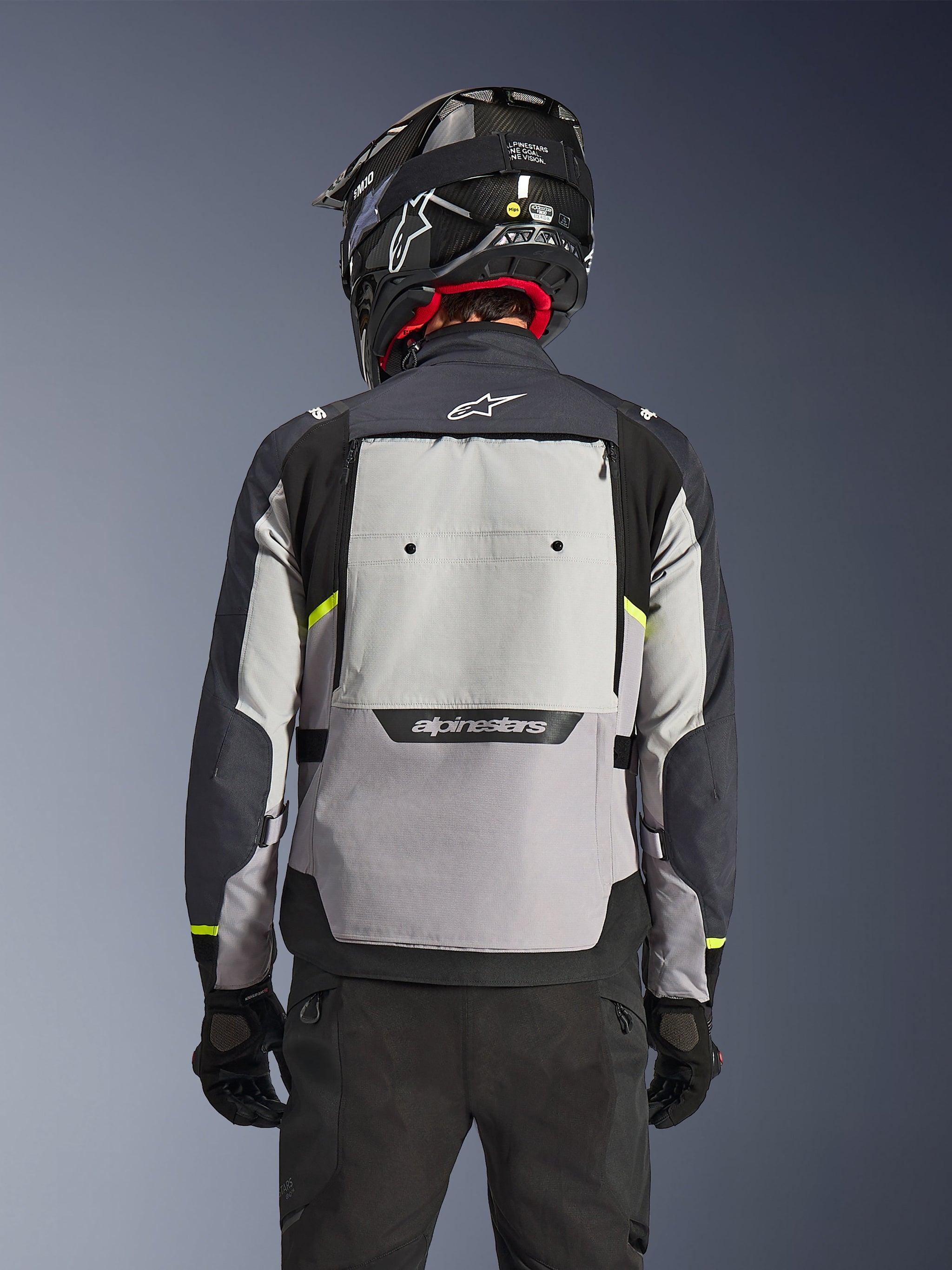 Alpinestars Cusco Drystar® Jacket, achteraanzicht, Ice Gray, Mid Gray en Deep Gray, voorzien van een groot ventilatiepaneel op de rug en felgele accenten, gecombineerd met een zwarte adventure-helm en zwarte broek.