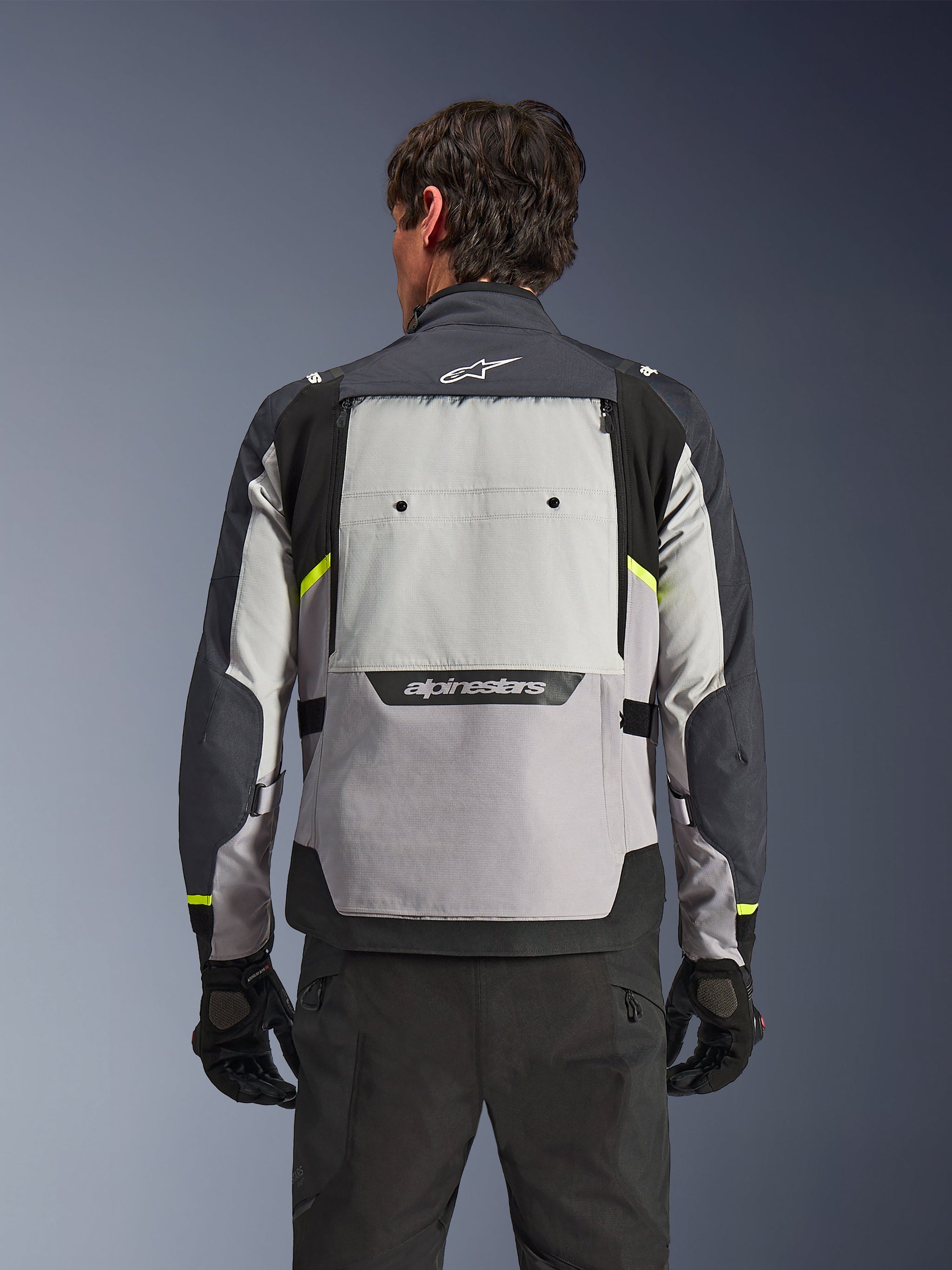 Alpinestars Cusco Drystar® Jas, achteraanzicht motorrijder, Ice Gray, Mid Gray en Deep Gray met neongele accenten, groot ventilatiepaneel op de rug, opvallende Alpinestars-branding, gecombineerd met zwarte motorbroek en handschoenen