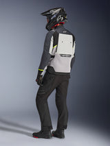 Alpinestars Cusco Drystar® Jas in Ice Gray, Mid Gray en Deep Gray, achteraanzicht op een motorrijder. Voorzien van fluorescerend gele accenten, een groot ventilatiepaneel op de rug met merkaanduiding en een duurzame textielconstructie. Gedragen met een zwarte motorbroek en een adventure-helm voor een complete touring-look.