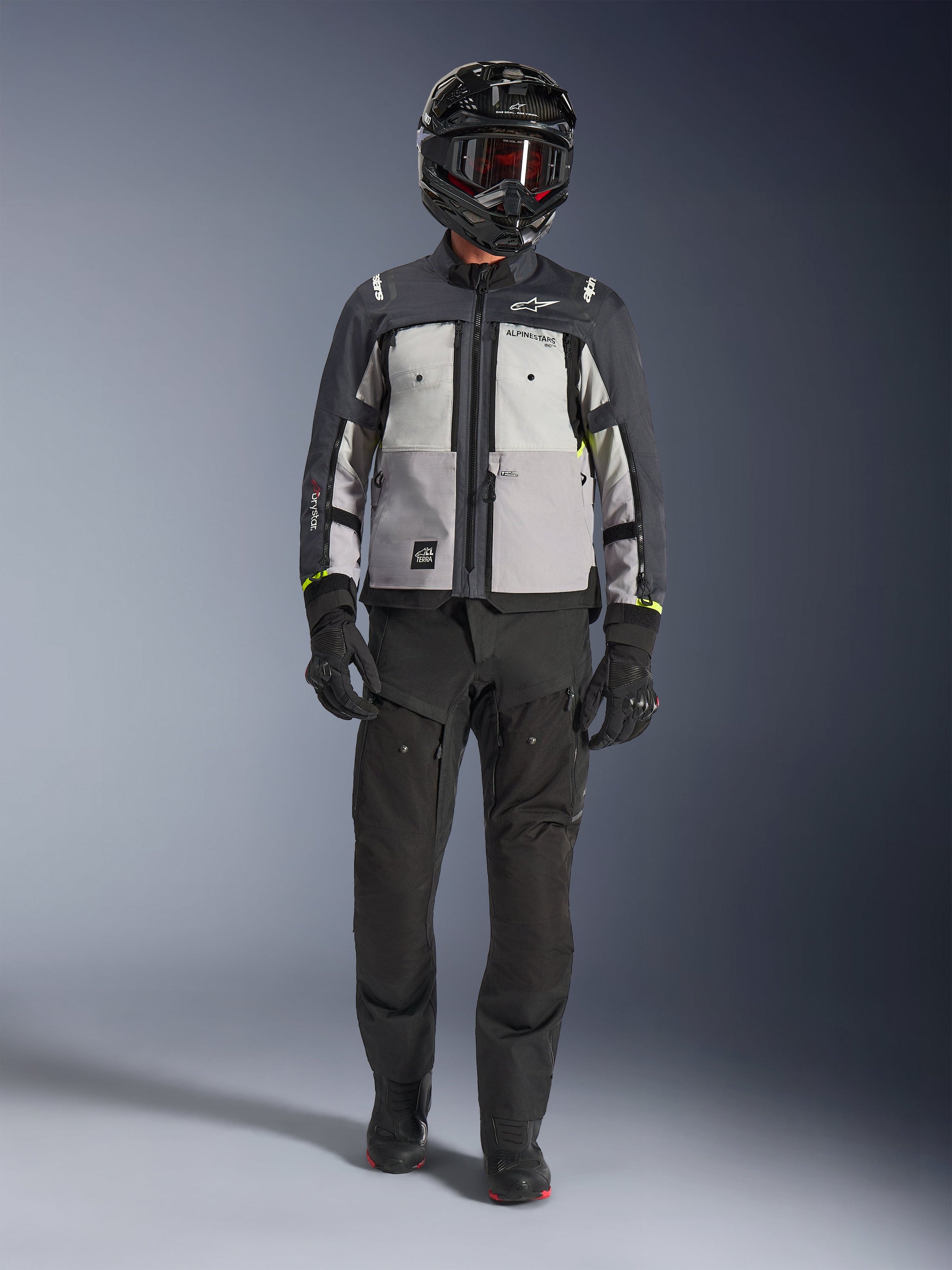 Alpinestars Cusco Drystar® Jas, Ice Gray Mid Gray Deep Gray, adventure motorjas gedragen met een zwarte motorbroek, zwarte handschoenen en een zwarte helm met motorbril, voorzien van grijze kleurvlakken en technische details voor road- en adventure-touring.