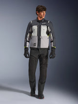 Alpinestars Cusco Drystar® Jacket in Ice Gray, Mid Gray en Deep Gray, gedragen met een zwarte adventure motorbroek en handschoenen, textiele adventure touring jas met multi-tonale grijze panelen en neongele accenten, studio-opname van een mannelijk model.