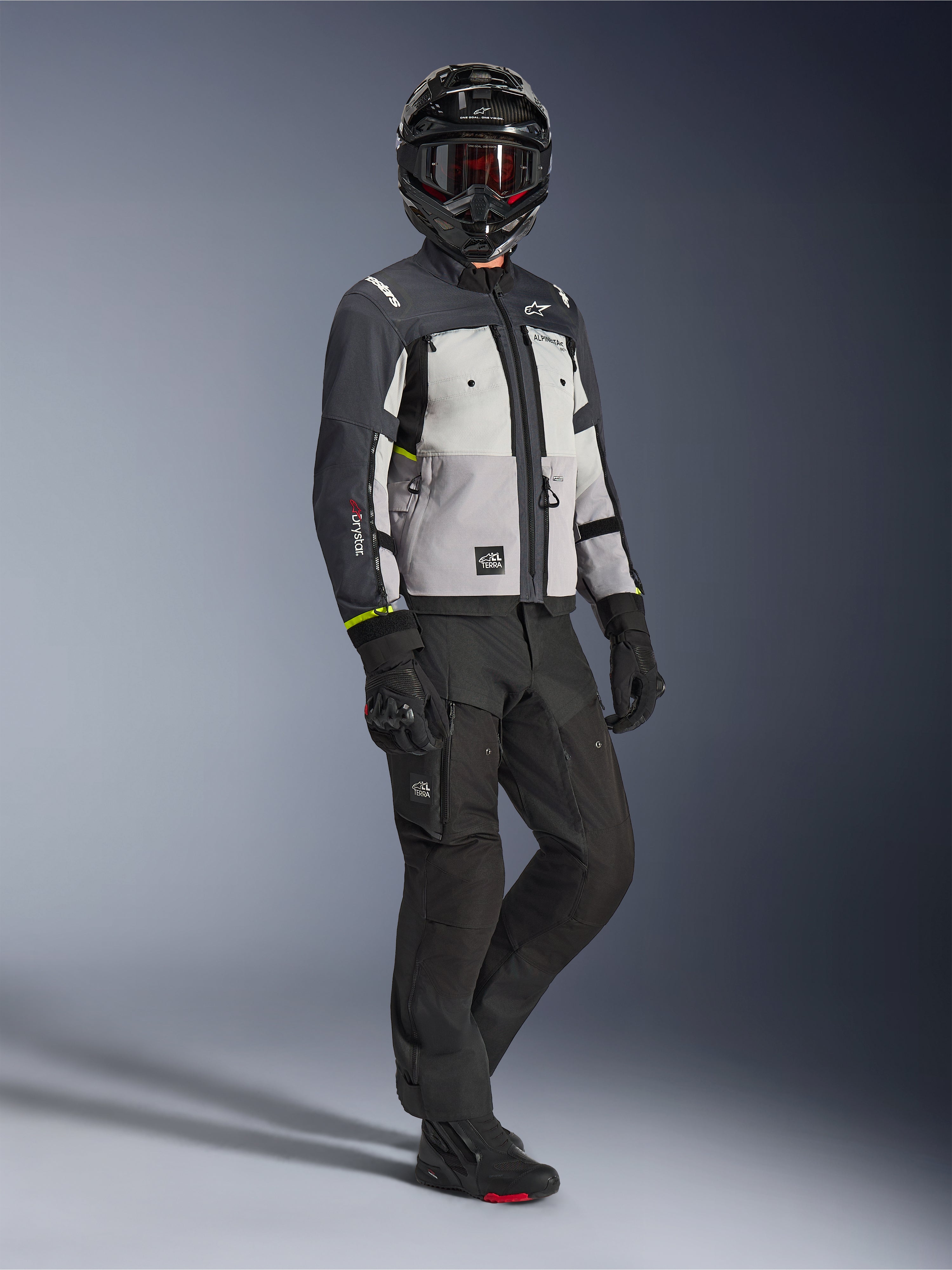 Alpinestars Cusco Drystar® Jacket in Ice Gray Mid Gray Deep Gray, full-body shot of a rider wearing complete adventure gear including a black helmet with red goggles, matching black pants, and gloves, textile motorcycle jacket with direct ventilation panels and waterproof membrane