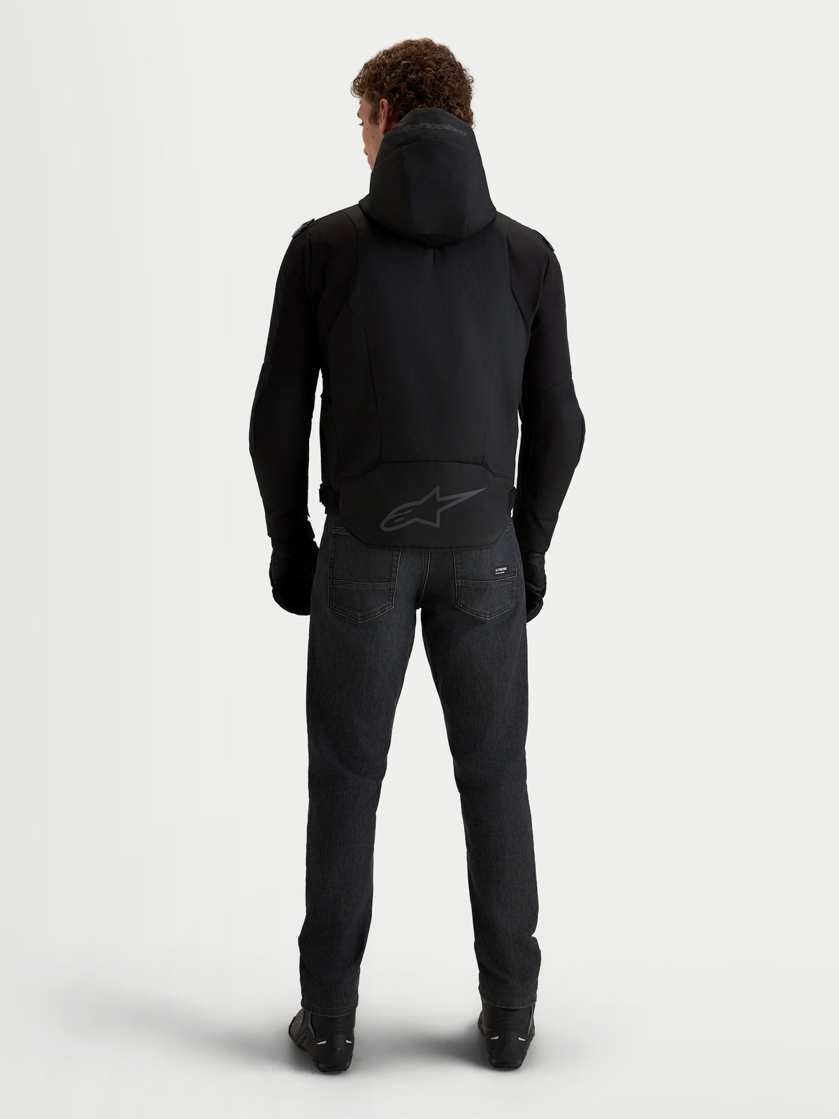 Alpinestars Zaca V2 Waterproof Jas, heren motorjas in het zwart vanaf de achterkant gezien, met vaste capuchon en verlengd rugpand met ton-sur-ton Alpinestars-logo