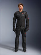 Mannelijk model met de Alpinestars ST-2 Air Jacket, zwarte motorjas met mesh-panelen en rood logo, 'Alpinestars Exploration Equipment'-tekst op de borst, gecombineerd met een zwarte technische rijbroek en handschoenen, moderne adventure touring-uitrusting