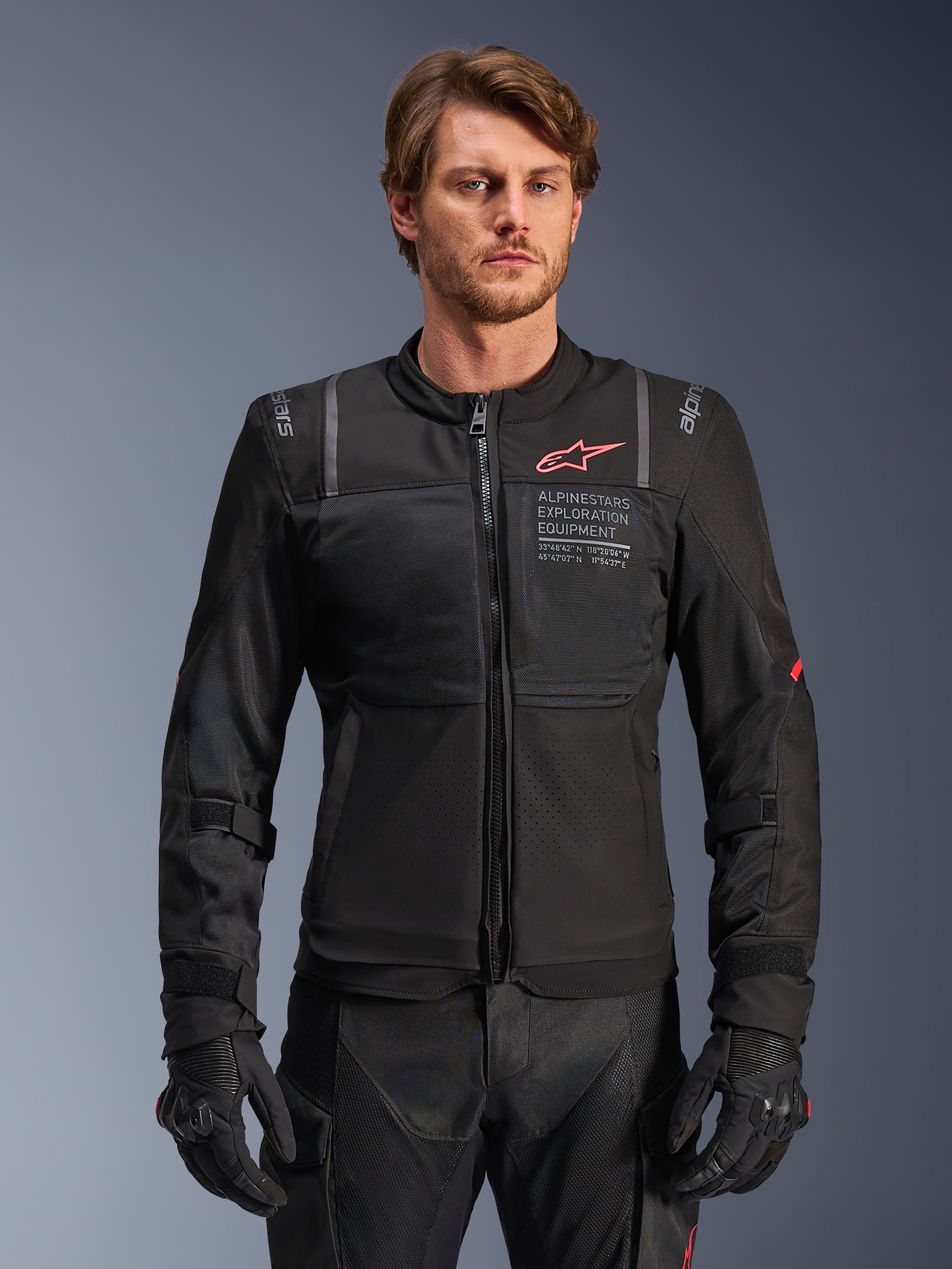 Alpinestars ST-2 Air Jacket, zwarte textiel motorjas voor heren, voorzien van grote mesh-panelen, rood Alpinestars-logo en "ALPINESTARS EXPLORATION EQUIPMENT" branding op de borst, gedragen door een mannelijk model met zwarte handschoenen en broek