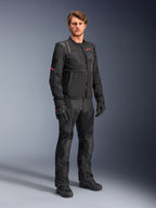 Mannelijk model in de zwarte Alpinestars ST-2 Air jas, voorzien van een rood ster-logo en 'Alpinestars Exploration Equipment' branding, gecombineerd met een bijpassende zwarte motorbroek, handschoenen en laarzen voor een moderne zomerse touring-outfit.