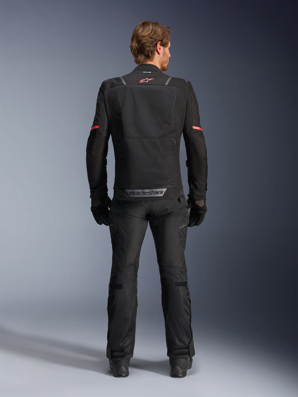 Alpinestars ST-2 Air motorjas, zwart, achteraanzicht van een motorrijder die de motorjas en bijpassende zwarte broek draagt, voorzien van mesh ventilatiepanelen, rood logo op de bovenrug en grijze Alpinestars-branding op de onderste zoom van de rug