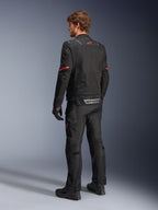 Alpinestars ST-2 Air Jacket, zwarte motorjas, achteraanzicht op model met een rood sterlogo op de bovenrug en reflecterende Alpinestars-branding bij de taille, gecombineerd met bijpassende zwarte technische motorbroek en handschoenen.