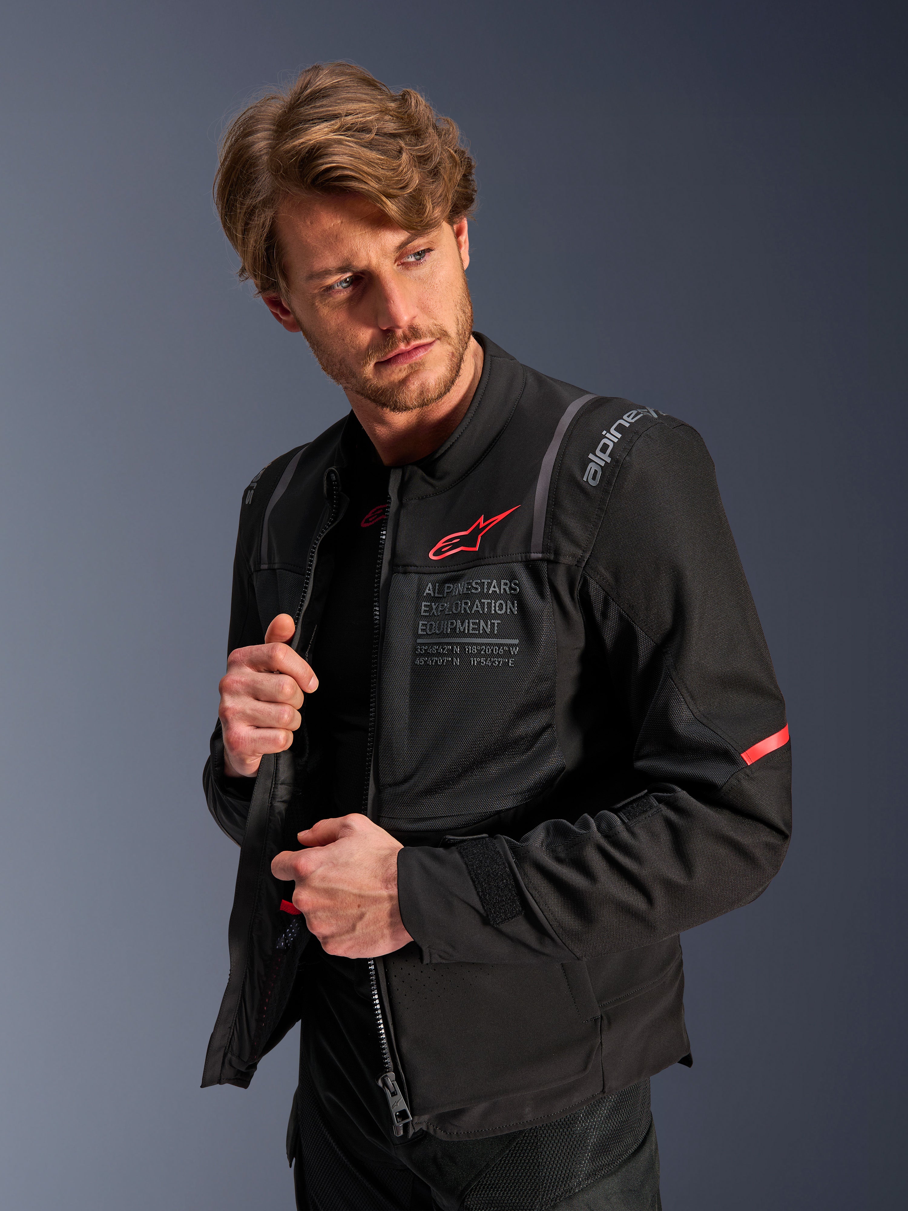 Alpinestars ST-2 Air Jacket, zwart, zomerse motor toerjas met grote meshpanelen, voorzien van een rood Astars-logo en 'Alpinestars Exploration Equipment' tekst op de borst, modern technisch ontwerp voor luchtstroom en bescherming, gedragen door een model