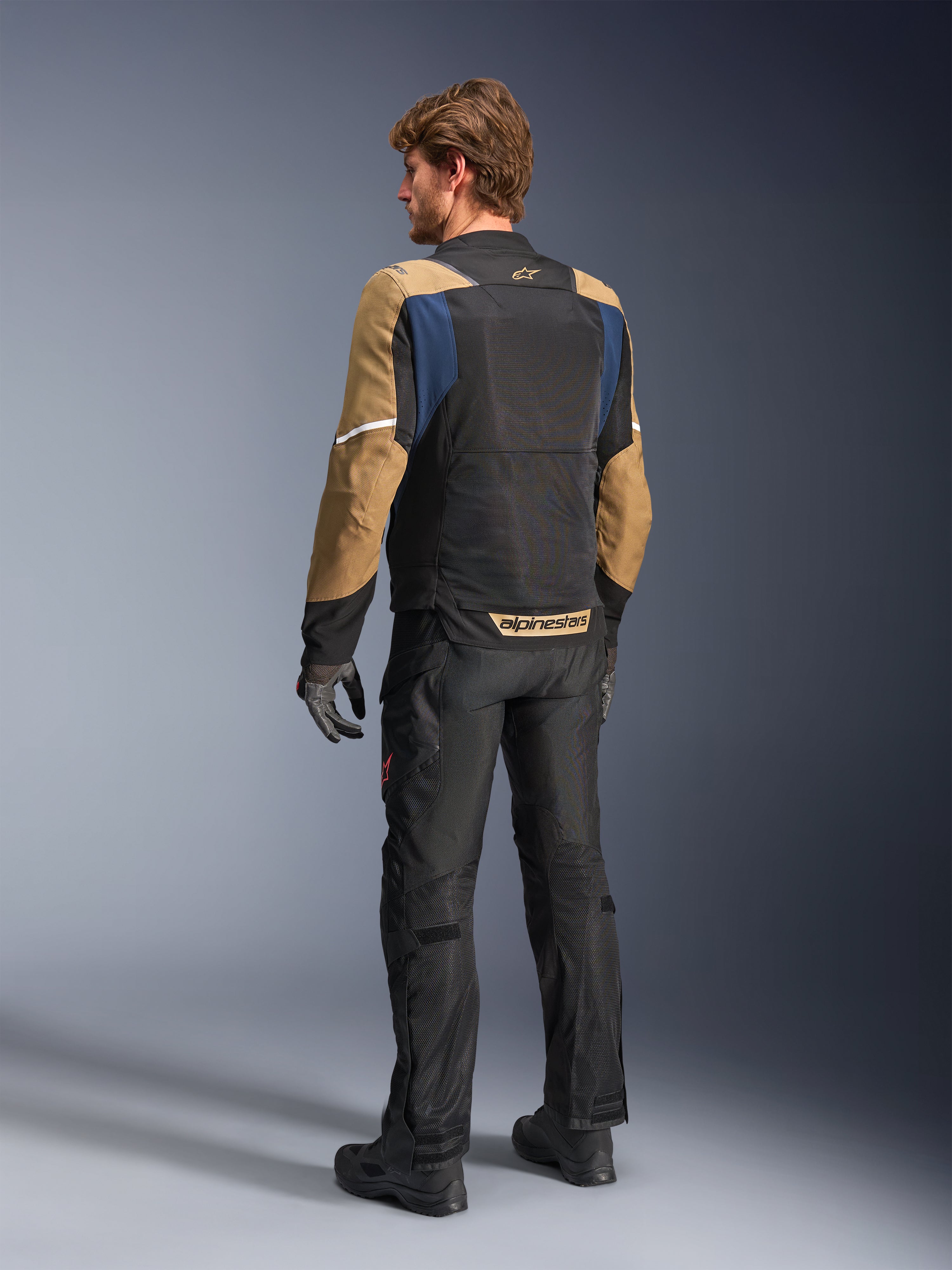Alpinestars ST-2 Air Jas, zomer touring motorjas, Deep Blue, Dark Khaki en zwart, achteraanzicht op model met mesh-panelen, khaki mouwen en blauwe accenten, voorzien van witte reflecterende strips en opvallende branding op de onderrug, gecombineerd met een zwarte motorbroek
