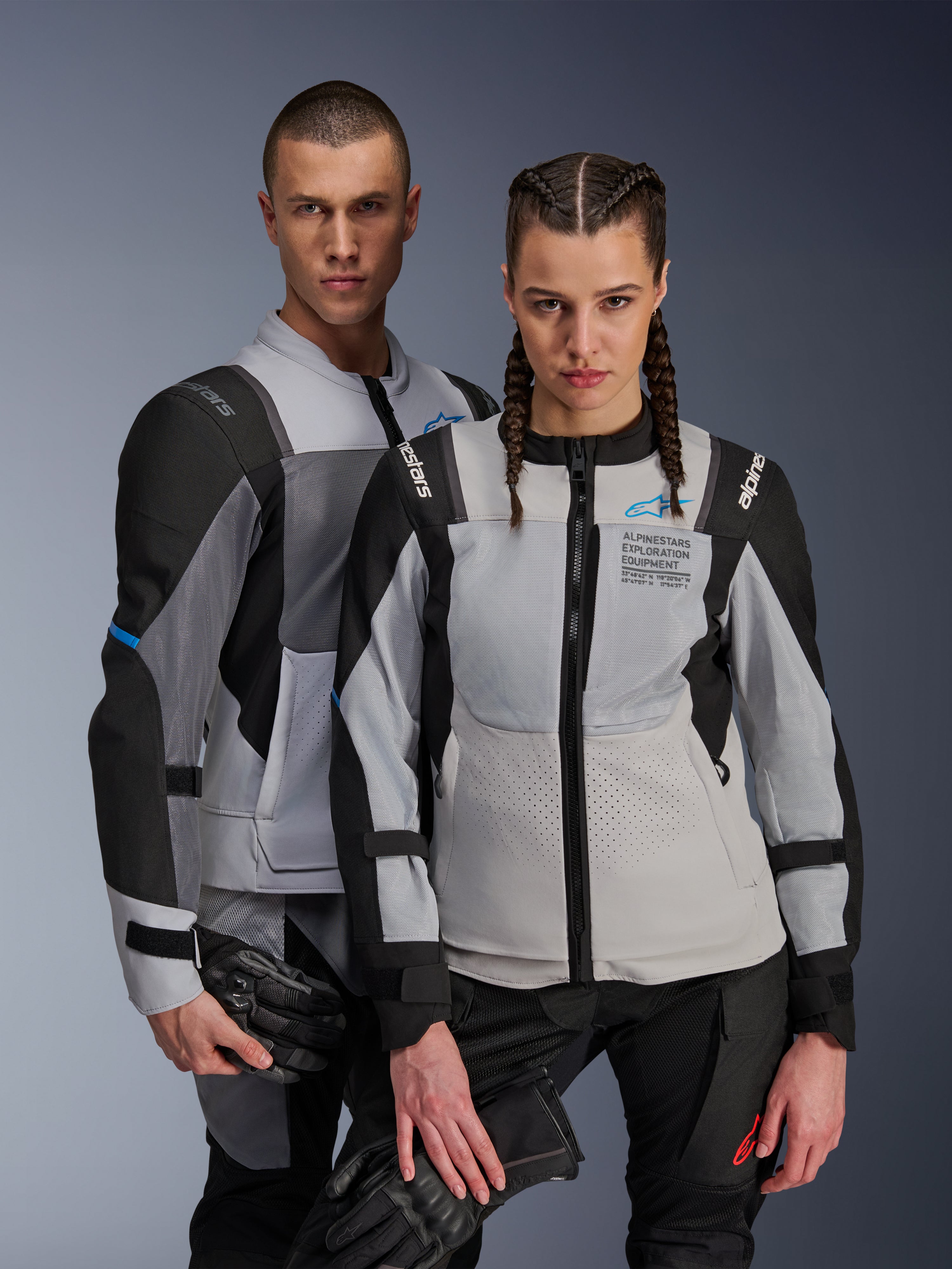 Alpinestars ST-2 Air jassen, textiele motorjassen, Ice Gray, donkergrijs en zwart, koppel draagt bijpassende adventure touring-uitrusting met mesh-ventilatiepanelen en Alpinestars Exploration Equipment-branding, houdt motorhandschoenen vast
