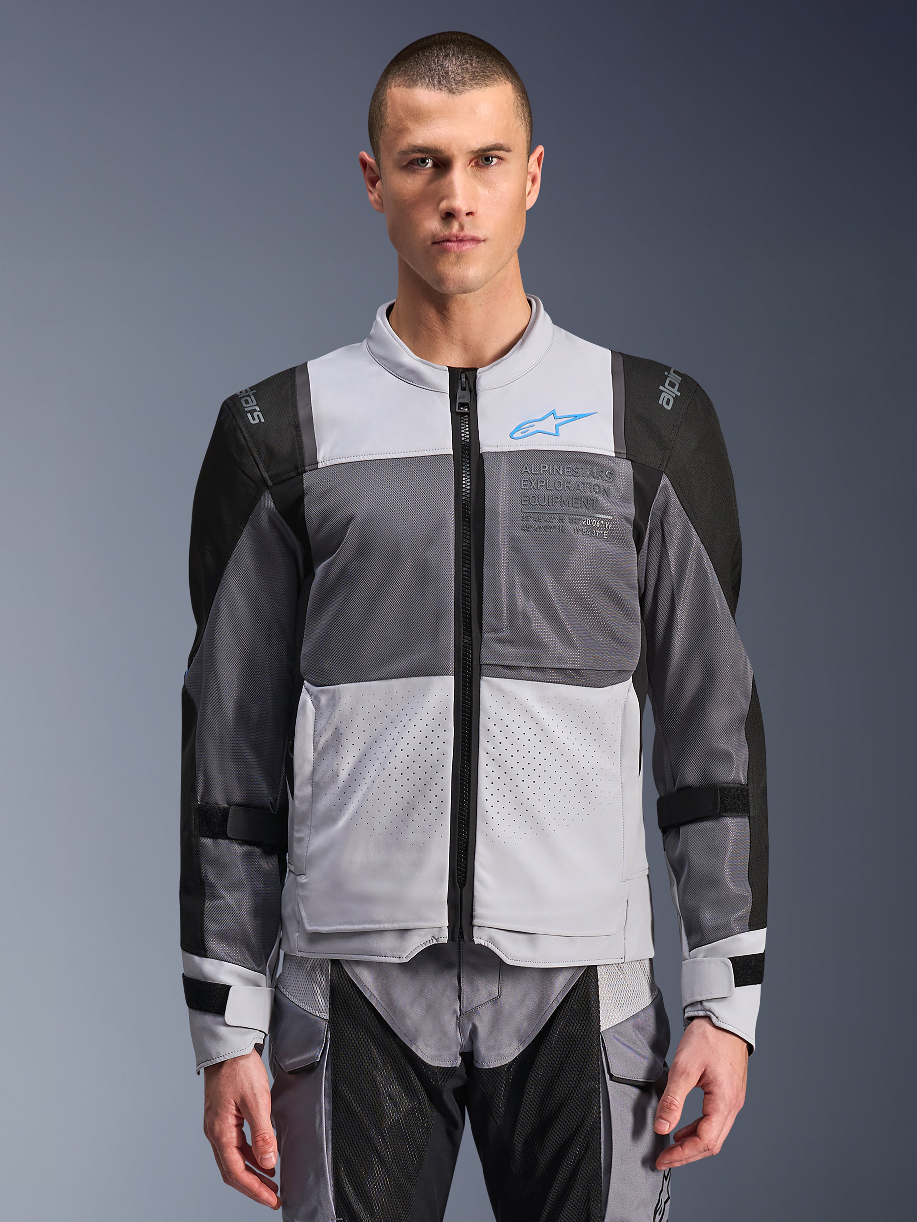 Alpinestars ST-2 Air Jacket, motorjas voor heren, ijsgrijs en donkergrijs met zwarte accenten, brede mesh-ventilatiepanelen, lasergeperforeerde voorzijde, blauw Alpinestars-logo, ritssluiting aan de voorzijde, gedragen door een model met bijpassende motorbroek