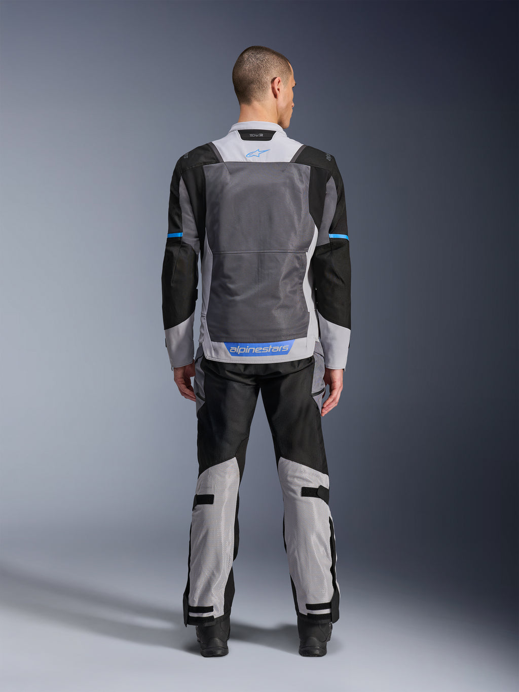 Alpinestars ST-2 Air Jas, Ice Gray Dark Gray Black, achteraanzicht op model, met grote mesh ventilatiepanelen, blauwe accenten en Alpinestars-logo, gecombineerd met bijpassende motorbroek voor adventure touring.