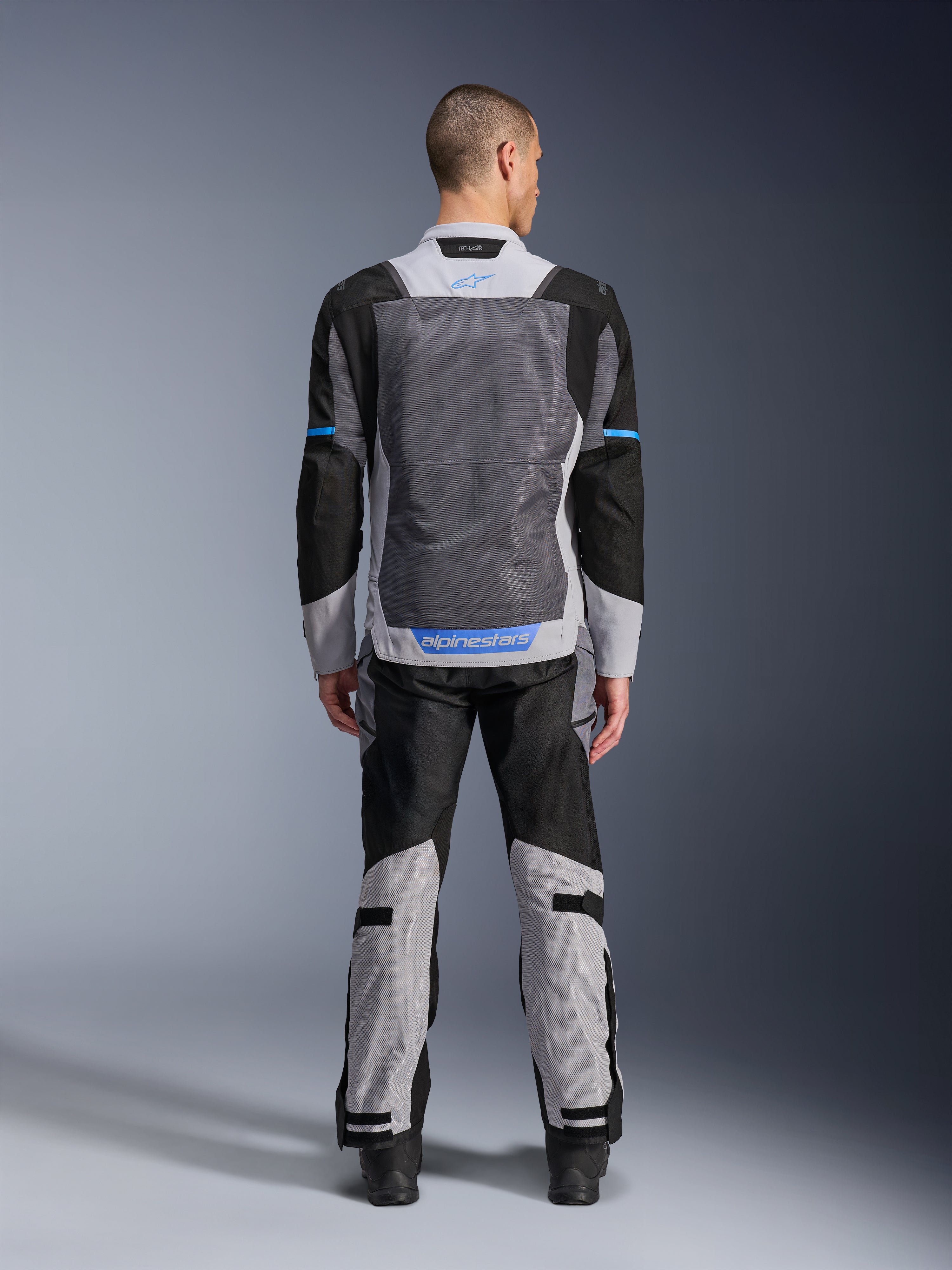 Alpinestars ST-2 Air Jas, Ice Gray Dark Gray Black, achteraanzicht op model, met grote mesh ventilatiepanelen, blauwe accenten en Alpinestars-logo, gecombineerd met bijpassende motorbroek voor adventure touring.