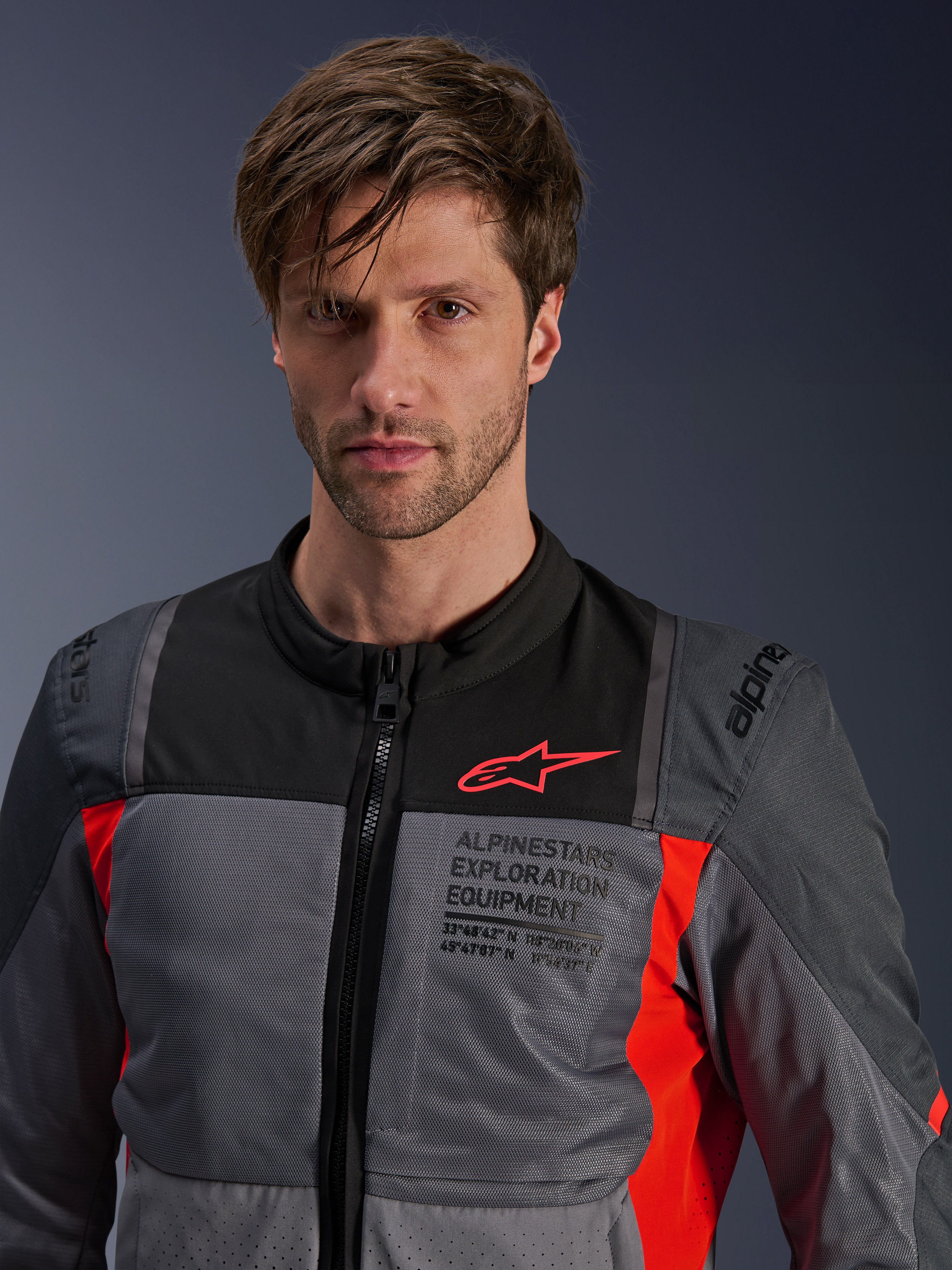 Alpinestars ST-2 Air jas, Deep Gray, Dark Gray en Bright Red, zomer touring motorjas gedragen door een model, voorzien van mesh ventilatiepanelen, rood Astars-logo en 'Exploration Equipment' branding op de borst
