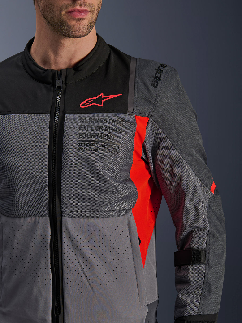 Alpinestars ST-2 Air Jacket, textiele motorjas, diepgrijs en donkergrijs met felrode details, close-up met ademende meshpanelen, lasergoperforeerde stof en rood sterlogo met Alpinestars Exploration Equipment-branding.