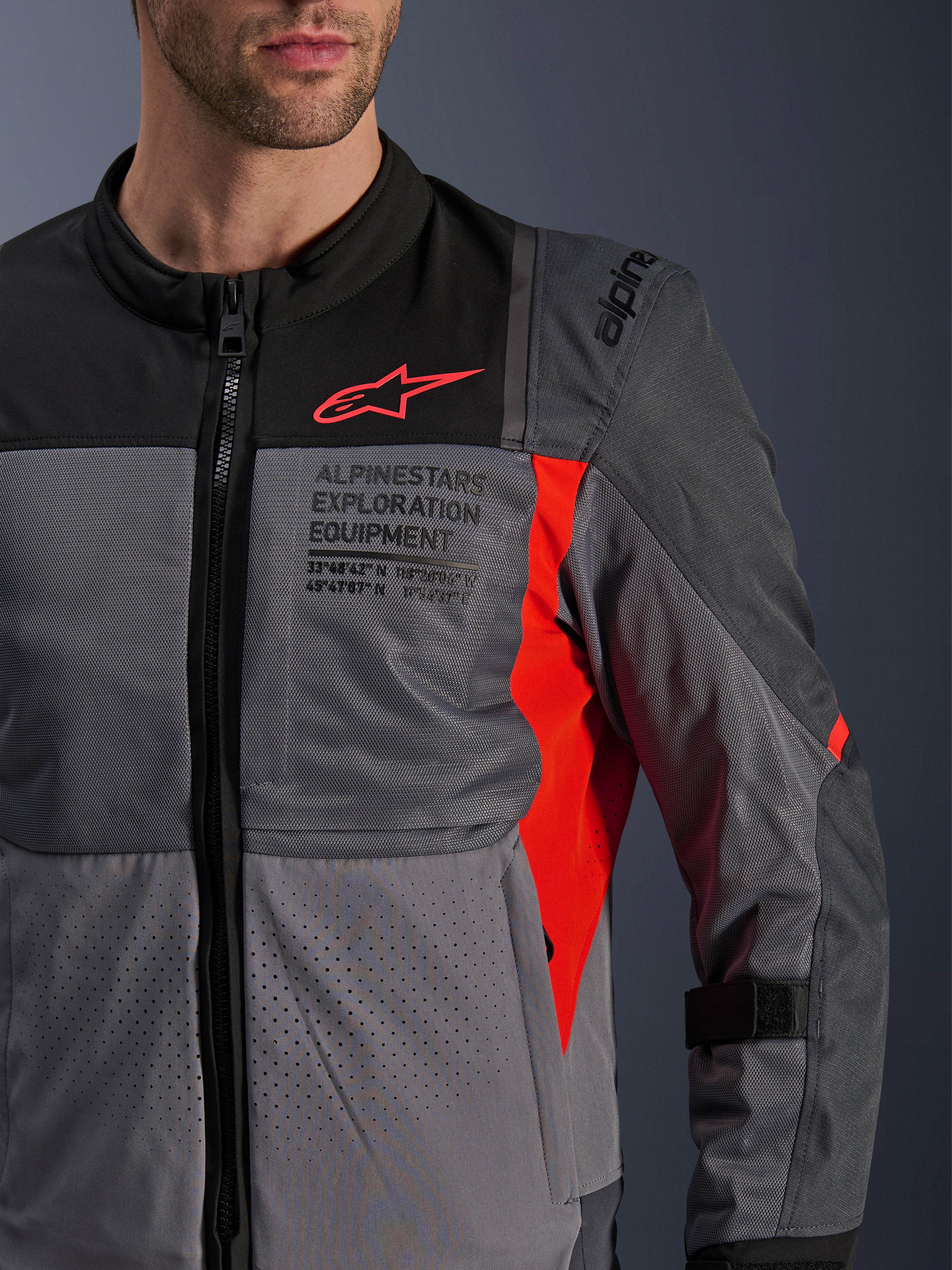 Alpinestars ST-2 Air Jacket, textiele motorjas, diepgrijs en donkergrijs met felrode details, close-up met ademende meshpanelen, lasergoperforeerde stof en rood sterlogo met Alpinestars Exploration Equipment-branding.