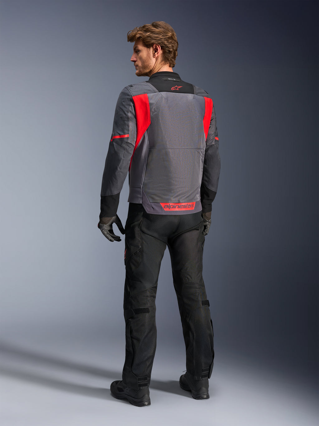 Alpinestars St-2 Air Jacket, motorjas, Deep Gray, Dark Gray en Bright Red, groot mesh ventilatiepaneel op de rug en rode branding, mannelijke rijder van achteren met zwarte motorbroek en grijze handschoenen