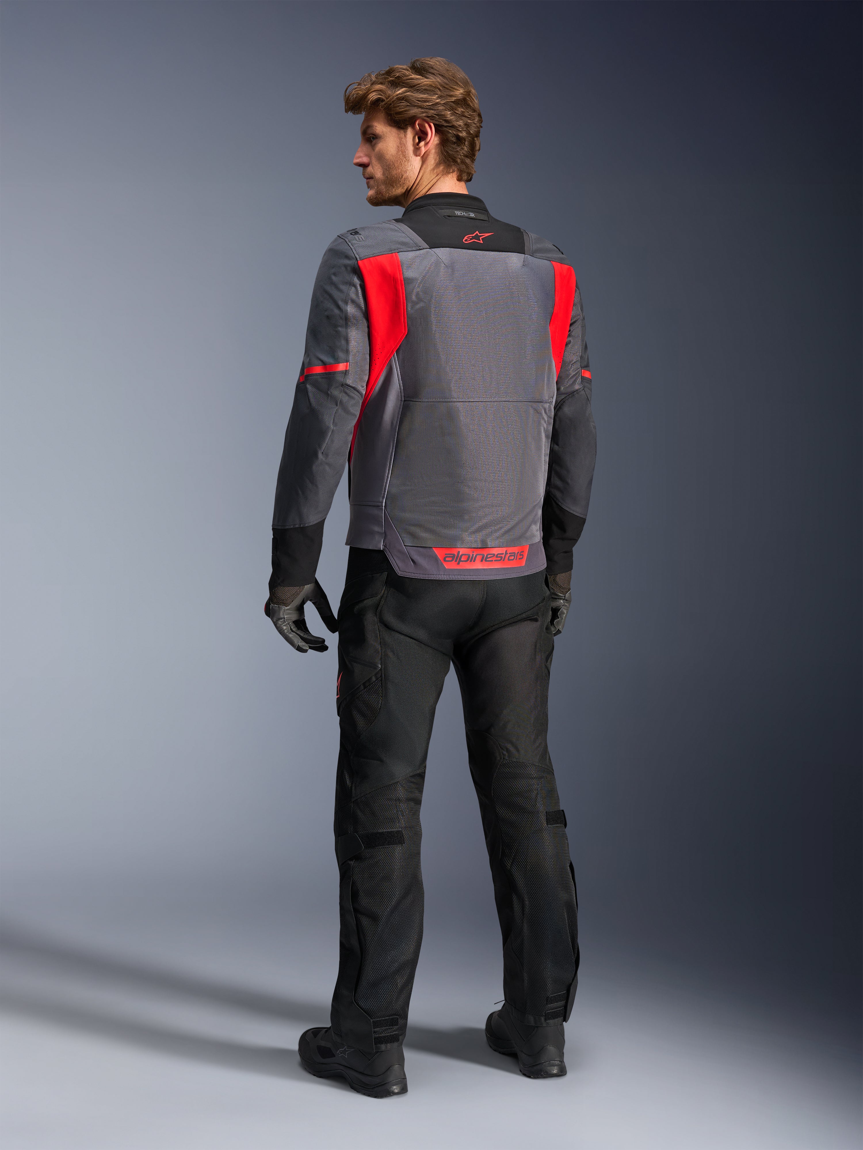 Alpinestars St-2 Air Jacket, motorjas, Deep Gray, Dark Gray en Bright Red, groot mesh ventilatiepaneel op de rug en rode branding, mannelijke rijder van achteren met zwarte motorbroek en grijze handschoenen