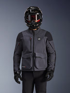 Alpinestars Maxdura Drystar®XF Laminated Armored Shell, motorjas, donkergrijs en zwart, gedragen door een rijder met een zwarte helm, bril en handschoenen, voorzien van grote technische cargozakken en ALL TERRA-branding, adventure touring uitrusting