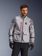 Alpinestars Maxdura Drystar®XF gelamineerde shell met protectie, adventure motorjas, middengrijs en donkergrijs met rode accenten, gedragen door een model met zwarte handschoenen en broek, voorzien van grote cargozakken en waterdichte ritsen, professionele motorkleding