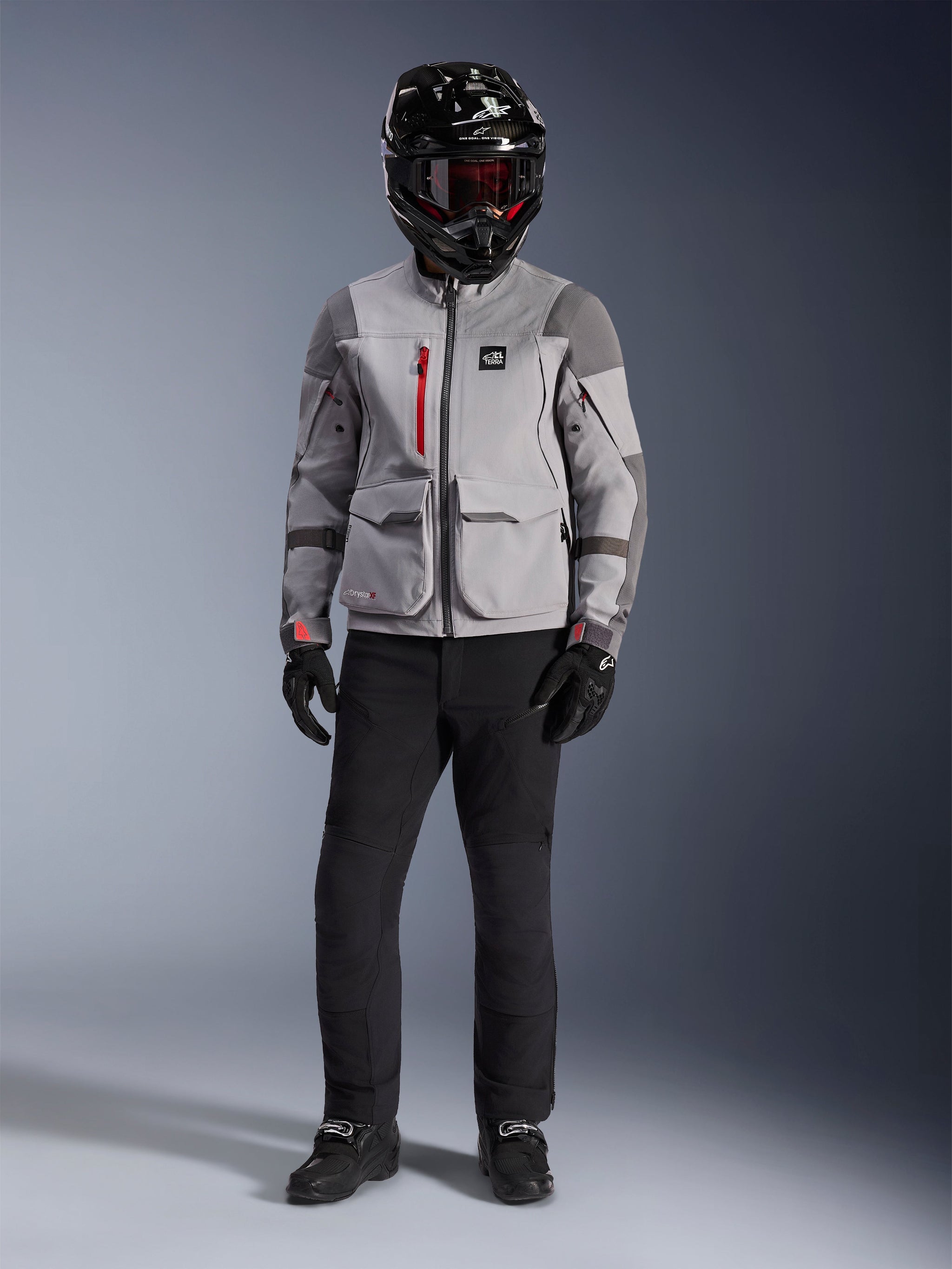Alpinestars Maxdura Drystar®XF Laminated Armored Shell, Mid Gray and Dark Gray adventure jacket with red zipper accents, worn by a rider with a black helmet, red goggles, and black pants, professional all-weather motorcycle gear