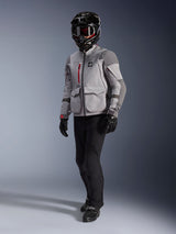 Adventure rider wearing the Alpinestars Maxdura Drystar®XF Laminated Armored Shell, Mid Gray and Dark Gray motorcycle jacket, black adventure helmet with goggles, black pants and gloves, featuring red zipper accents and cargo pockets, technical gear for adventure touring.