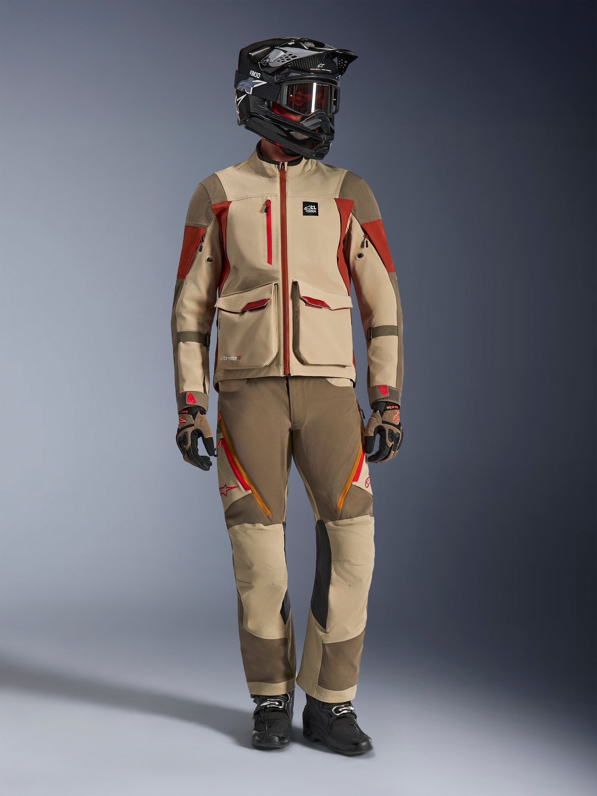 Alpinestars Maxdura Drystar®XF Laminated Armored Shell Jacket in Aluminum Walnut Rust Brown, bijpassende adventure broek, zwarte off-road helm met roodgetinte bril, technische handschoenen, volledige adventure touring outfit, studio-opname van een rijder.