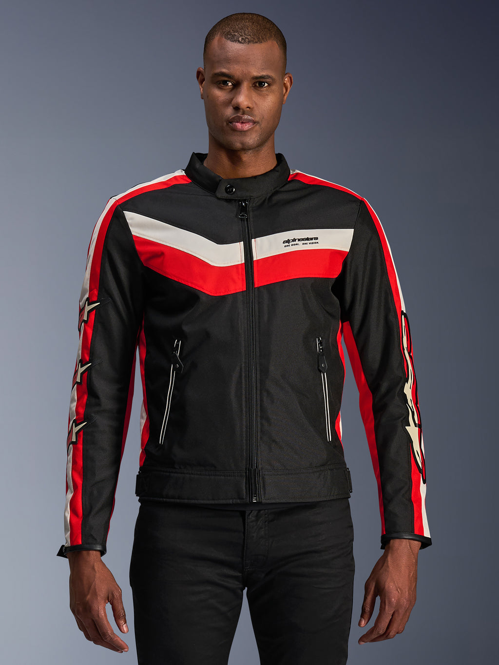 Alpinestars T-Dyno WR jas, textiele motorjas, zwart met felrode en ecru chevron-strepen, vintage-geïnspireerde biker-pasvorm, hoge kraag met knoopsluiting, voorzakken met ritssluiting, sterlogo's op de mouwen, gedragen door model