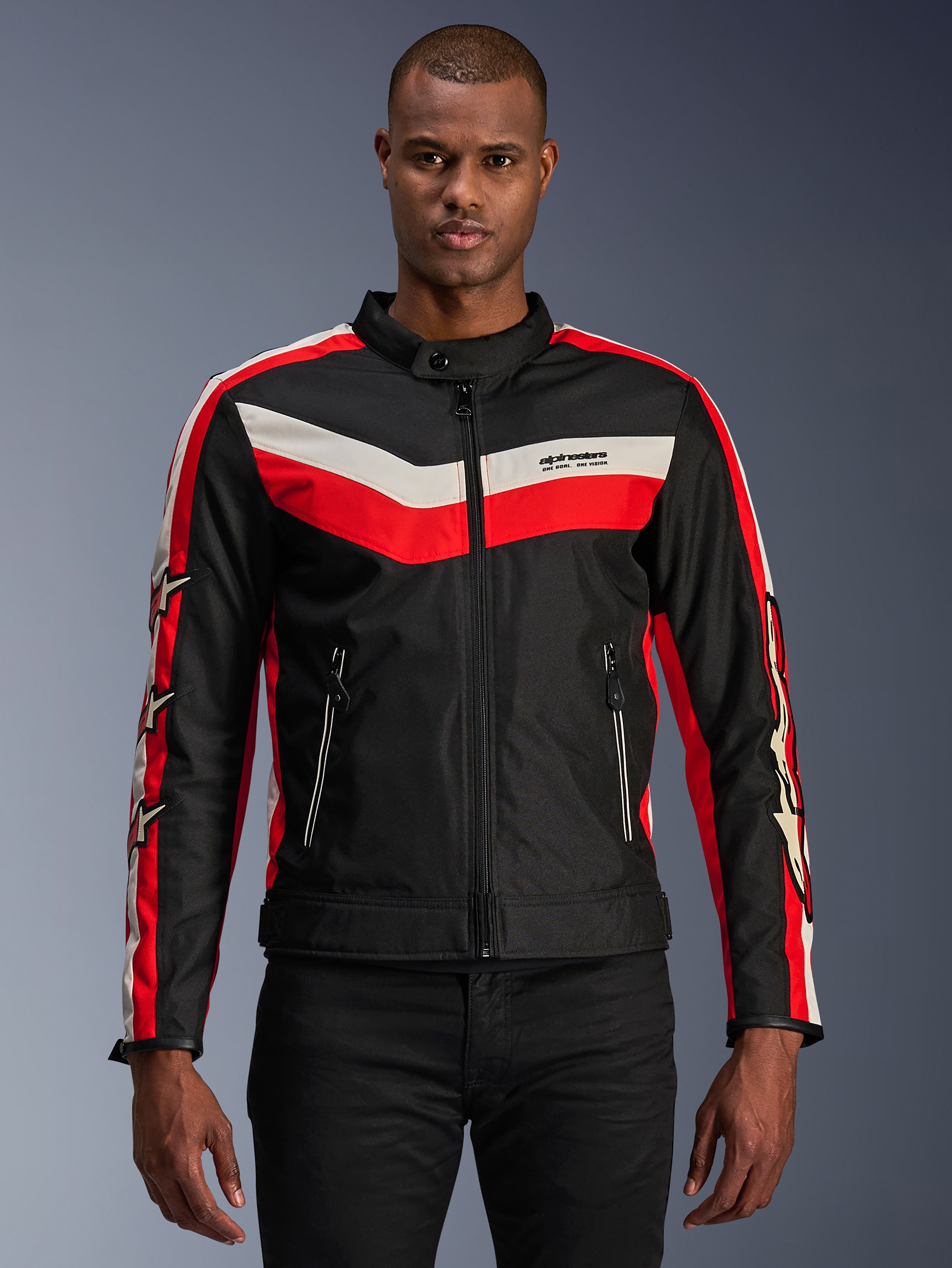 Alpinestars T-Dyno WR jas, textiele motorjas, zwart met felrode en ecru chevron-strepen, vintage-geïnspireerde biker-pasvorm, hoge kraag met knoopsluiting, voorzakken met ritssluiting, sterlogo's op de mouwen, gedragen door model