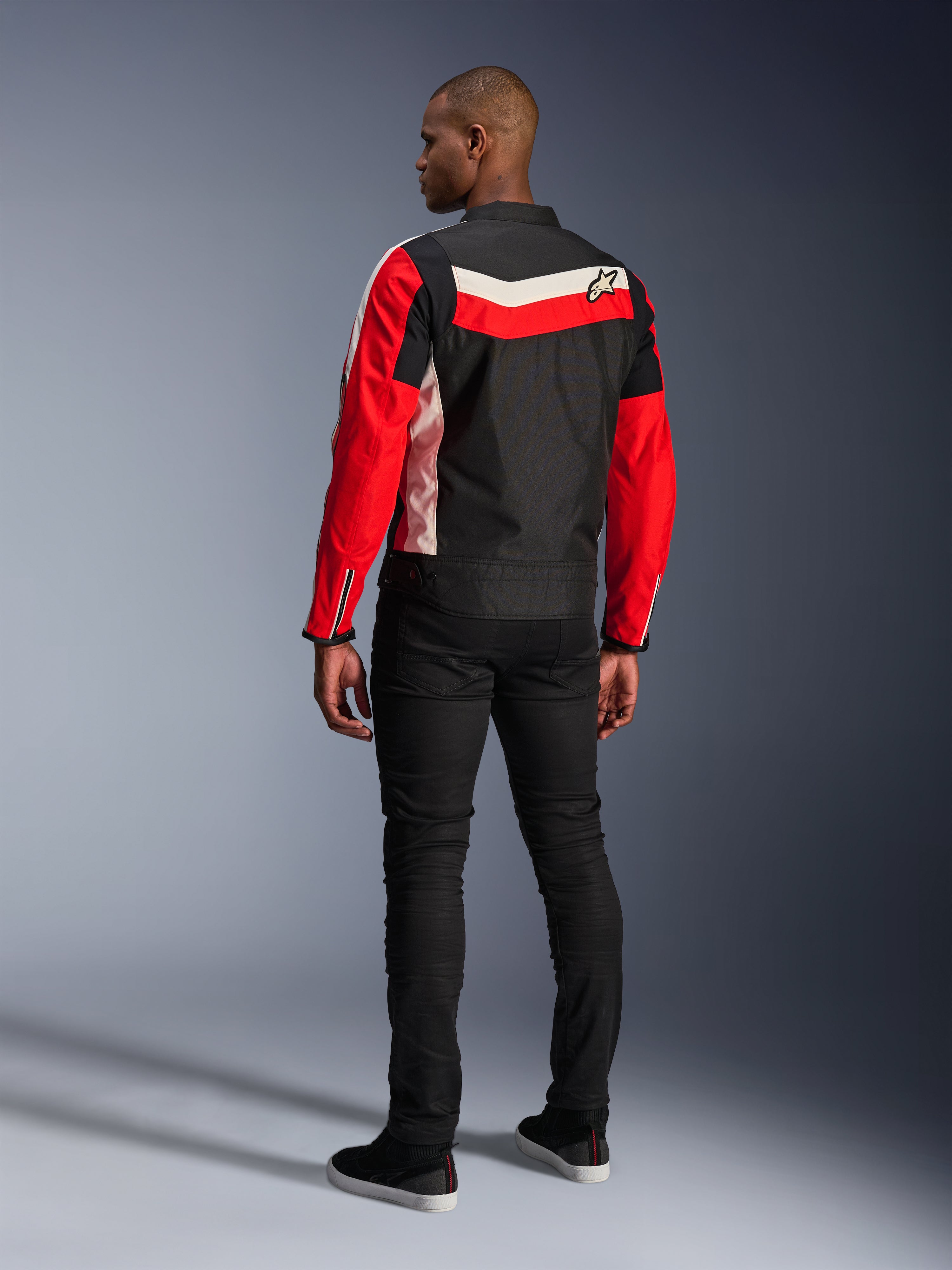 Alpinestars T-Dyno WR Jacket, textiele motorjas, zwart, helderrood en ecru, achteraanzicht op model, vintage-geïnspireerde biker pasvorm met erfgoed kleurpanelen en logo, moderne urban motorkleding.