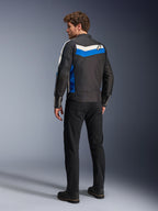 Alpinestars T-Dyno WR jas in Black Blue Ecru, achteraanzicht op een mannelijk model, voorzien van een witte en blauwe chevronstreep over de schouders met een ster-logo, vintage-geïnspireerde textiele motorjas, gedragen met een zwarte broek en laarzen