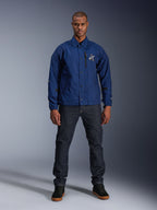 Alpinestars Revved WR Jas, marineblauw, motorjas in coach-stijl, gedragen door een man met donkere denim jeans en zwarte sneakers, voorzien van drukknoopsluiting en 3D Alpinestars-logo, urban contemporary streetwear