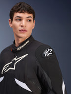 Alpinestars T-GP R V3 Drystar® jas, zwart en wit, gedragen door een mannelijk model, voorzien van witte Alpinestars-logo's op de kraag en borst, zwarte DFS-schouderslider met een witte ster, gedetailleerde lifestyle-foto van een waterdichte sportieve textieljas