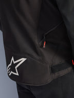 Alpinestars T-GP R V3 Drystar® Jacket, zwart en wit, detailopname van de onderrug met een groot wit Alpinestars sterlogo, een zijzak met rits en rood lipje, en een klittenband verstelband in de taille, gemaakt van duurzaam textiel.