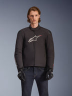 Alpinestars SMX Waterproof Jacket, Black textile motorcycle jacket with white and red star logo on the chest, worn by a model with black gloves and blue jeans, featuring external shoulder sliders and a sporty fit.