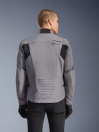 Alpinestars SMX Waterproof jas, grijs met zwarte accenten, achteraanzicht met branding op de bovenrug en verlengd achterprofiel, gedragen door een model met zwarte broek en handschoenen