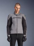 Alpinestars SMX Waterproof Jacket, sportieve motorjas, donkergrijs en zwart, met een hoge kraag en DFS Lite schoudersliders, gedragen met zwarte SMX-handschoenen, strakke atletische pasvorm voor rijden in alle weersomstandigheden