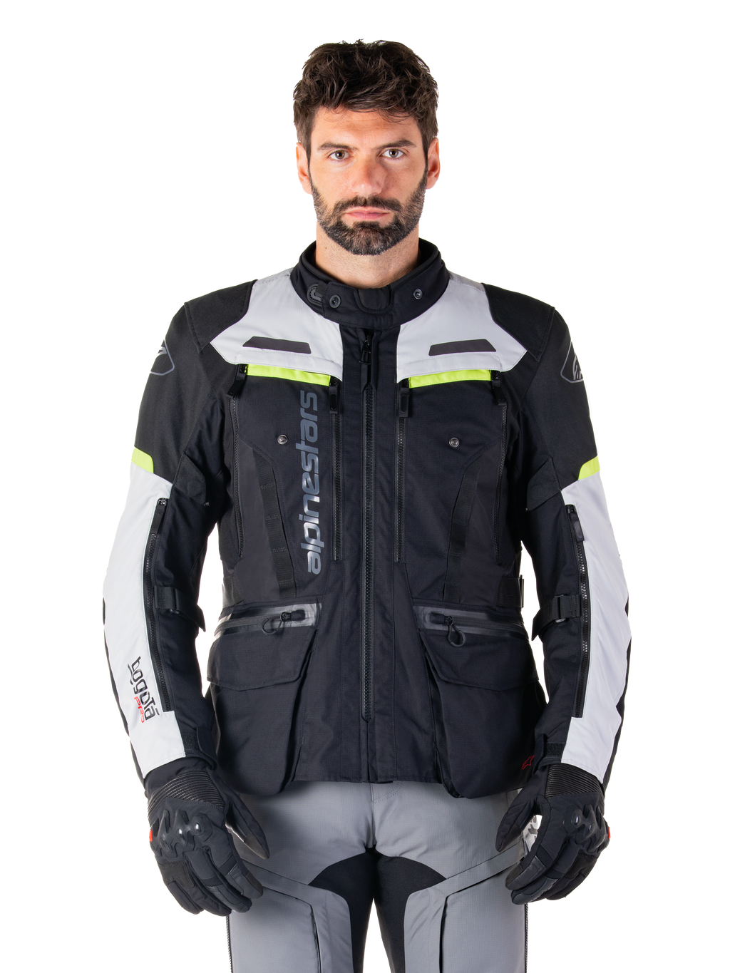 Man draagt een Alpinestars Bogotá Pro Drystar® Jas, Black Ice Gray en Yellow Fluo, all-season adventure touring motorjas, waterdicht ontwerp met meerdere zakken en verticale branding, gecombineerd met zwarte handschoenen en een grijze motorbroek